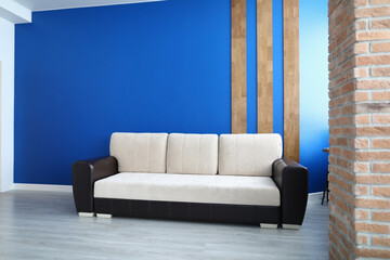 Close-up of comfy sofa for office or living room. Stylish white colour and black insert. Bright blue wall with wooden lines decoration. Laminate on floor. Comfort and trendy interior design concept