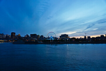 A skyline of Montreal Old Port and Downtown at the twilight blue hour. Foreground is Saint Laurent river.