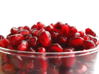 Pomegranate with seeds in a glass bowl isolated on a white background.