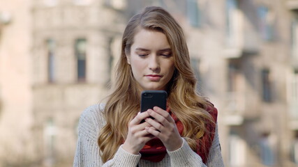 Beautiful woman using phone outdoors. Pretty girl looking phone screen on street