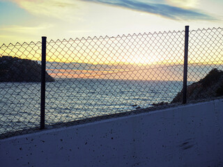 Sunset through wire fence. Pink sunset on promenade.