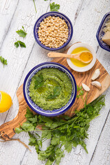 Homemade parsley pesto sauce and ingredients on white  wooden background.