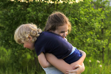 Fototapeta premium Cute teenager girl and little blonde boy playing and laughing on a green meadow. Sister and brother, siblings. Summertime, family concept. 