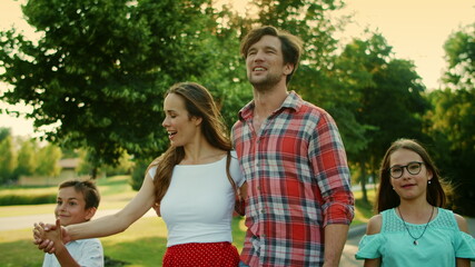 Children and parents walking in summer park. Father holding daughter hand