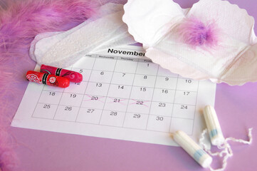 Menstrual pads and tampons on menstruation period calendar with on lilac background.