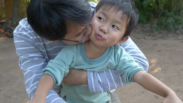 4K Asian child boy and dad in happy moment shot, smiling with happy cute face outdoor, hug and kiss with love. Father's day and son concept, slow motion shot.