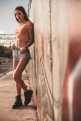 Ritratto intero di giovane ragazza affascinante in abiti casual estivi mentre posa lungo un viale di una strada urbana di città - obrazy, fototapety, plakaty