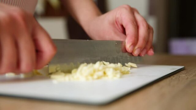 girl cuts garlic with a knife on the board. woman in the kitchen chopped peeled garlic