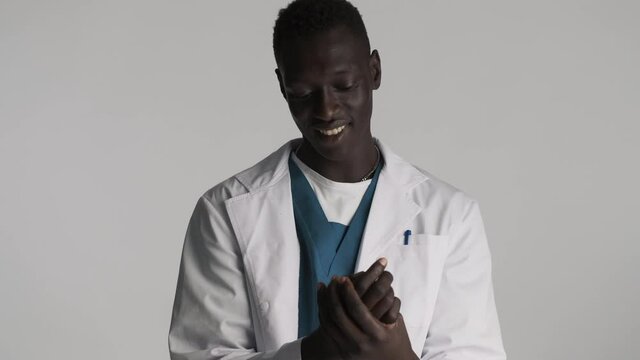 Young attractive African American male doctor happily wash his hands over gray background. Safety first