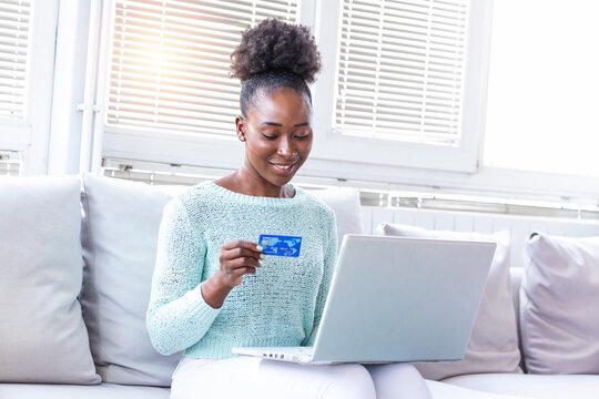 Young woman holding credit card and using laptop computer. Online shopping concept. Happy black woman doing online shopping at home