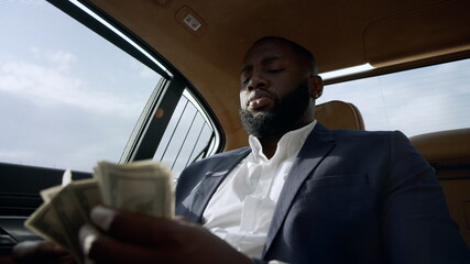 Closeup african man counting money at car. Businessman sitting with money at car
