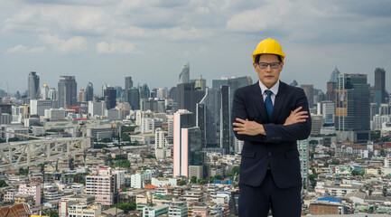 The Asian male business executive wears a hard hat and stands to watch the real estate development project with confidence in his success.