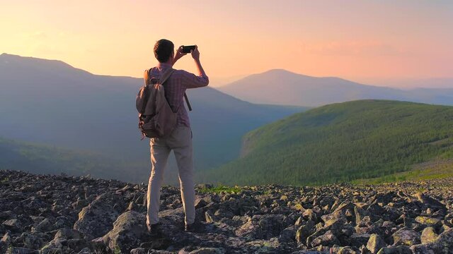 A man in the mountains photographs the landscape on his smartphone. A tourist with a backpack photographs the sunset on a mountain pass. Hiking in the mountains of the Northern Urals.