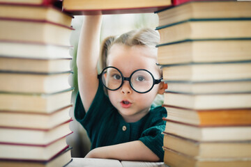 Beautiful little blonde kid girl in round shaped glasses 4-6 years old among many books. Kid education concept