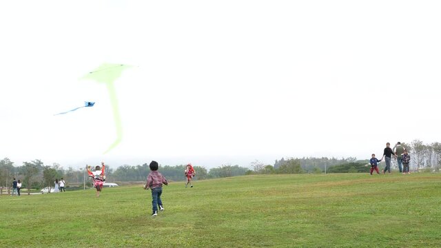 4K Asian child boy playing kite and running in park in nature background. Happy fun family activity in winter holiday, freedom and travel concept.