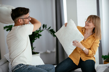 Young couple fighting pillows on the bed. Happy couple having fun at home.	
