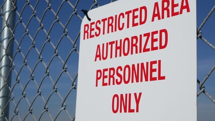 Restricted area, authorized personnel only sign in USA. Red letters, keep off warning on metal fence, United States border symbol. No trespassing notice means violators will be prosecuted by US law