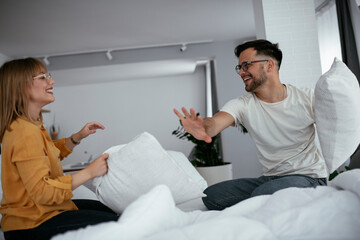 Obraz premium Young couple fighting pillows on the bed. Happy couple having fun at home. 