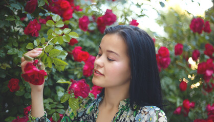 brunette woman smiling in a flowering bush of red roses