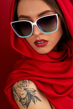Portrait of beautiful brunette sexy girl with luxurious make-up in white sunglasses and red headscarf on red background