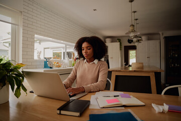 Woman entrepreneur sitting at home working on laptop with business documents on the table