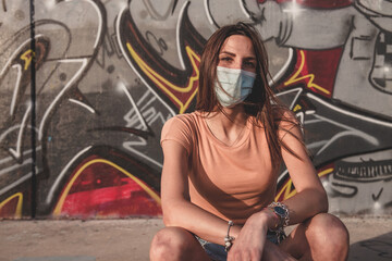 Giovane ragazza affascinante con sguardo serioso indossa la mascherina seduta su uno sfondo urbano 