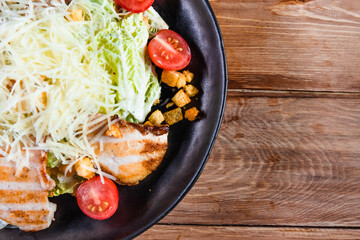 Appetizing Caesar salad with chicken in a black plate on a wooden table. The concept of healthy food and serving