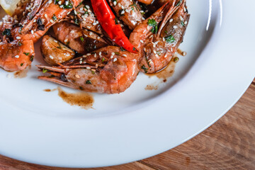Appetizing fried shrimp with specialties, sesame seeds and lemon, on a white plate on a background of wood. Food concept in restaurants and bars