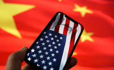 Chinese american economic relationship concept: View on hand holding mobile phone with USA flag....