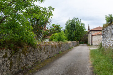 Fototapeta na wymiar Rural road view with trees and stone wall, with a small church in the background, in Cantabria, Spain, horizontal