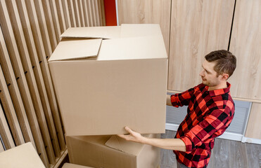 Young man, a courier, is carrying a cardboard box in a post office store.