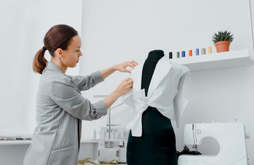 Young woman tailor is arranging a future shirt on a mannequin in her mini workshop.