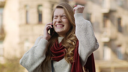 Happy woman hearing great news by phone outdoors. Excited girl using smartphone.