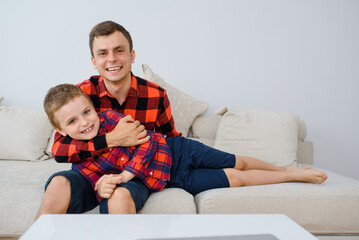 Laughing father and his son, in same plaid shirts are playing and having fun.