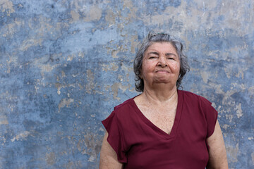 Portrait of an elderly woman dressed a wine color blouse with a blue rustic wall background