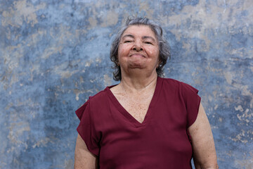 Fototapeta premium Portrait of an elderly woman dressed a wine color blouse with a blue rustic wall background