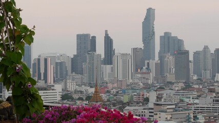 View of traditional and modern buildings of oriental city. Beautiful flowerbed against cityscape of traditional houses and skyscrapers on misty day on streets of Bangkok or Krungtep.