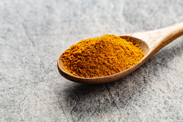 Turmeric powder in wooden spoon on grey concrete background close-up with copyspace