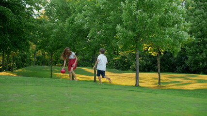 Fototapeta premium Mother and children playing with ball in meadow. Family enjoying time outside