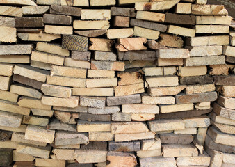 A large pile of cut wooden boards arranged along a wall