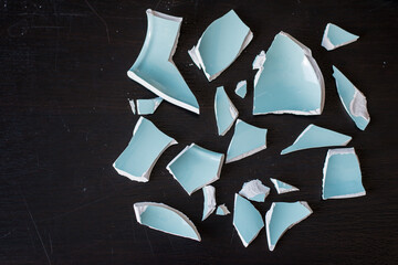 Shards of a broken light blue vase on a black surface