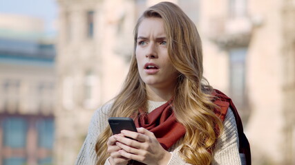 Upset woman using phone outside. Stressed girl looking around on city street