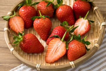 Tasty red fresh organic strawberries inside a bamboo plate with napkin on wooden background.