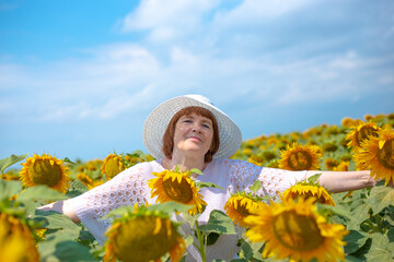 european woman pensioner stands in a field with blooming sunflowers, arms outstretched to the sides, lifestyle