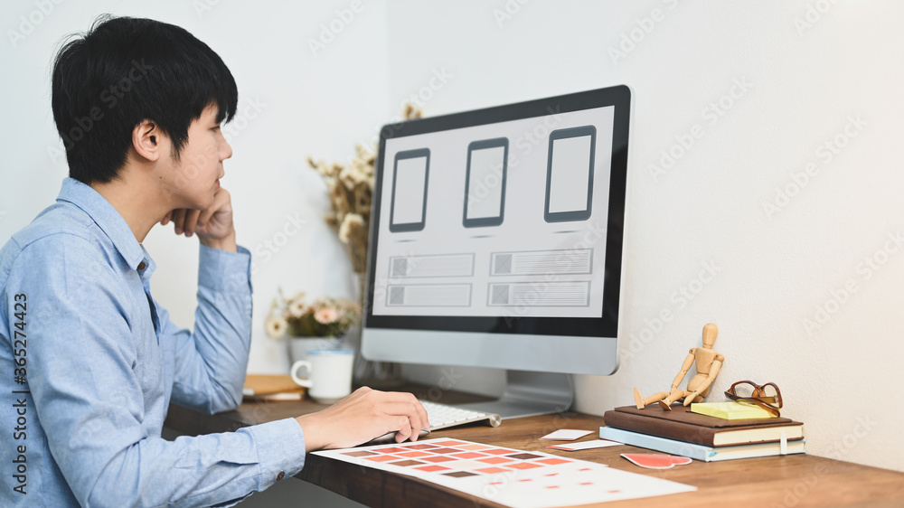Aufkleber the graphic designer is working with a computer at the wooden working desk.