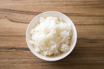 Bowl of boiled rice on wooden background, top view with space for text