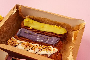 Box with fresh eclairs on pink background