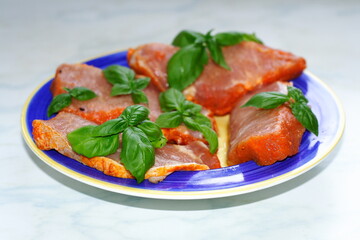 Pieces of beautiful red pork, prepared for grilling, on a blue plate, with green basil