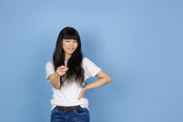 Pointing on, choosing you. Portrait of young asian woman isolated on blue studio background. Beautiful cute girl in casual. Human emotions, facial expression, sales, ad, online shopping concept.