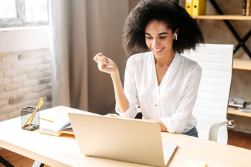 Cheerful young African-American businesswoman working in an office. Exited biracial girl smiles and looks at the laptop screen